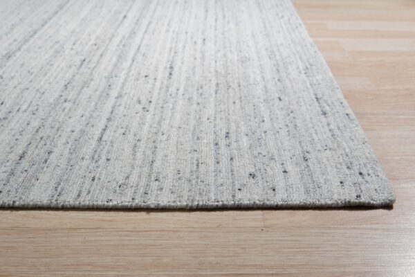 Close-up of a low-pile gray speckled rug with faint vertical stripes on light wood planks.