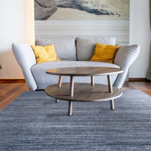 A blue rug with horizontal white stripes grounds a round wooden coffee table and a gray sofa.