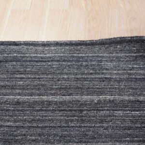 Textured dark gray rug featuring faint horizontal striping on a blonde wood floor.