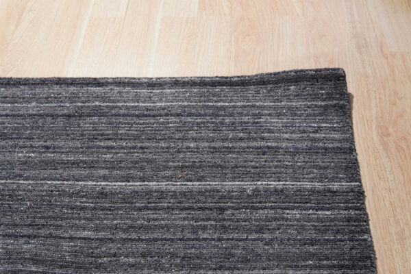Textured dark gray rug featuring faint horizontal striping on a blonde wood floor.