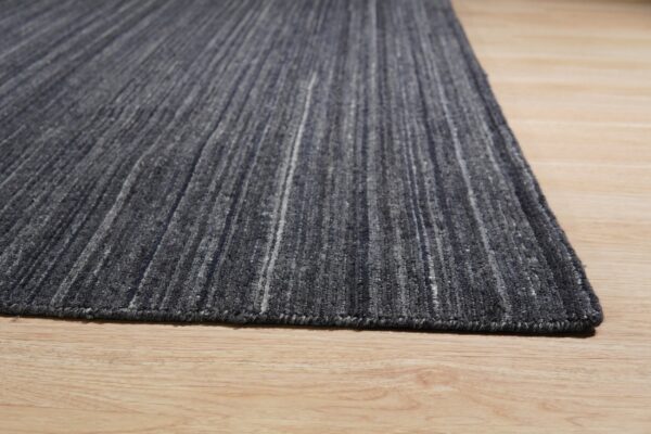 Gray textured rug with light vertical streaks covers light wood plank flooring.