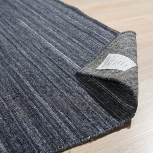 Dark blue variegated rug is curled on light wood planking, exposing the gray woven backing.