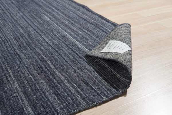 Dark blue variegated rug is curled on light wood planking, exposing the gray woven backing.