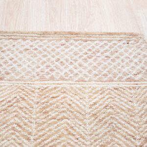 Light tan and cream rug with geometric and chevron patterns rests on blonde wood flooring.