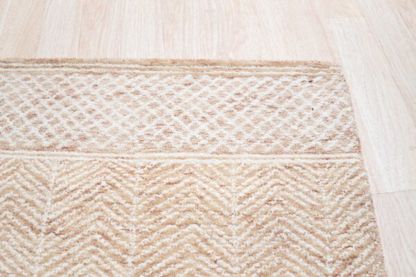 Light tan and cream rug with geometric and chevron patterns rests on blonde wood flooring.
