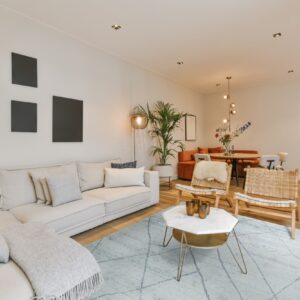 A light blue low-pile geometric rug grounds a modern living room with a beige sofa and wood chairs.