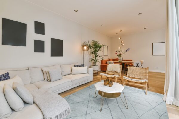 A light blue low-pile geometric rug grounds a modern living room with a beige sofa and wood chairs.