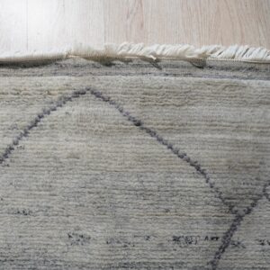 Shaggy cream rug featuring dark, thin diamond patterns and long fringe on pale hardwood flooring.
