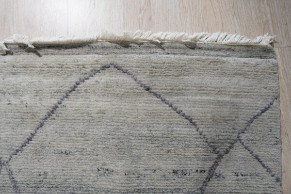 Shaggy cream rug featuring dark, thin diamond patterns and long fringe on pale hardwood flooring.