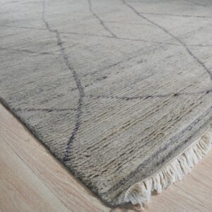 Shaggy cream rug featuring thin dark gray lines and fringe rests on light wood plank flooring.