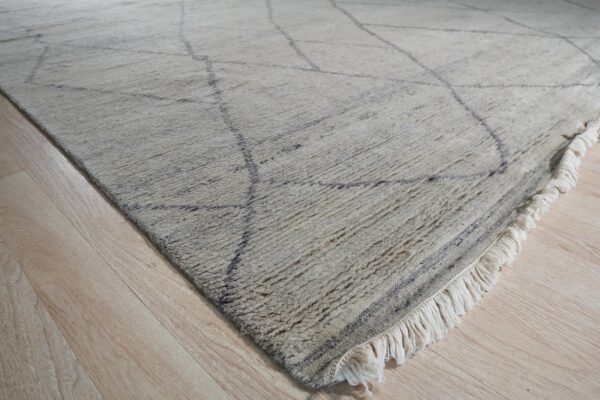Shaggy cream rug featuring thin dark gray lines and fringe rests on light wood plank flooring.