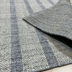 Striped gray and cream rug with varied textures lies on a wooden floor, revealing its flat woven backing.