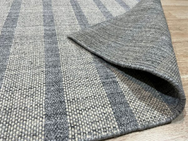 Striped gray and cream rug with varied textures lies on a wooden floor, revealing its flat woven backing.