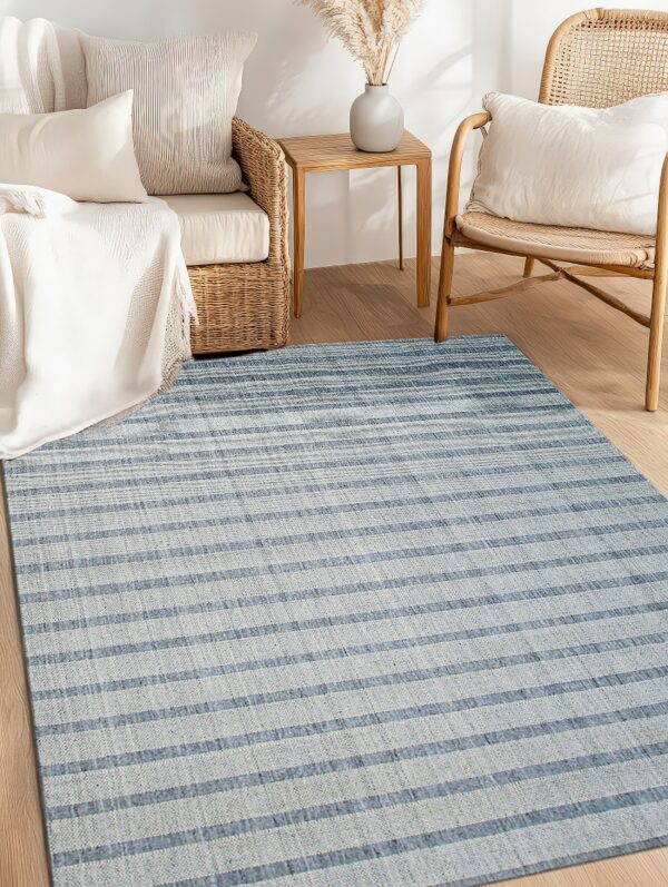 A blue and light gray low-pile striped rug is laid beneath natural wicker and wood furniture.