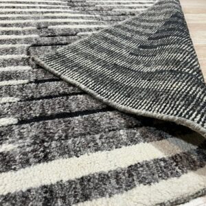 A striped black and white high-pile rug is rolled back to expose the woven underside on wood flooring.