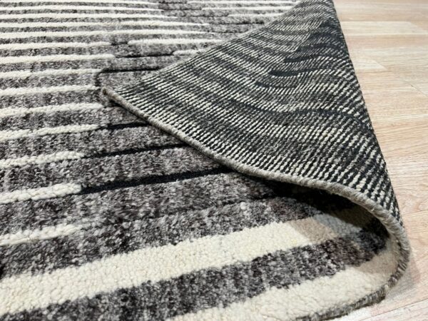 A striped black and white high-pile rug is rolled back to expose the woven underside on wood flooring.