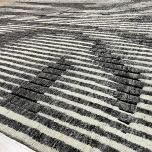Carved high-low pile rug with thick off-white and charcoal stripes lying on light wood planks.