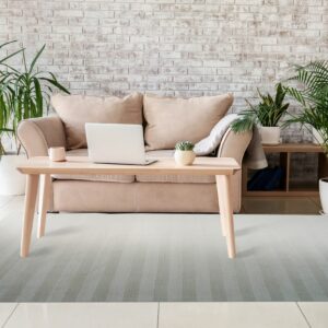 A low-pile grey striped rug rests on light tile under a wooden table and tan sofa.