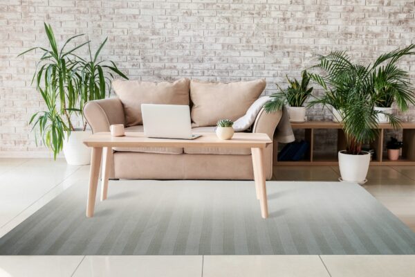 A low-pile grey striped rug rests on light tile under a wooden table and tan sofa.