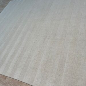 Light neutral area rug featuring tone-on-tone vertical stripes on plank wood flooring.