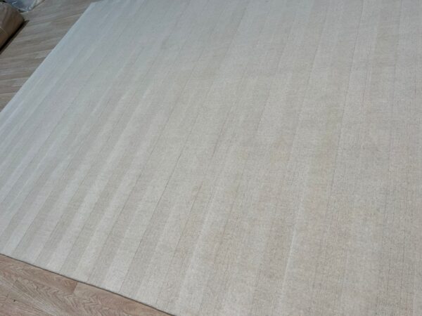 Light neutral area rug featuring tone-on-tone vertical stripes on plank wood flooring.