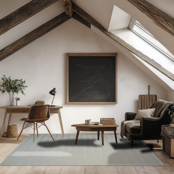 A pale gray rug covers wood flooring in an attic room furnished with a desk and dark armchair.