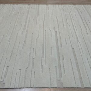 Light beige plush rug with tone-on-tone carved vertical lines resting on wood planks.