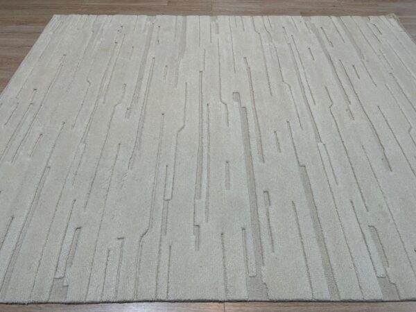 Light beige plush rug with tone-on-tone carved vertical lines resting on wood planks.