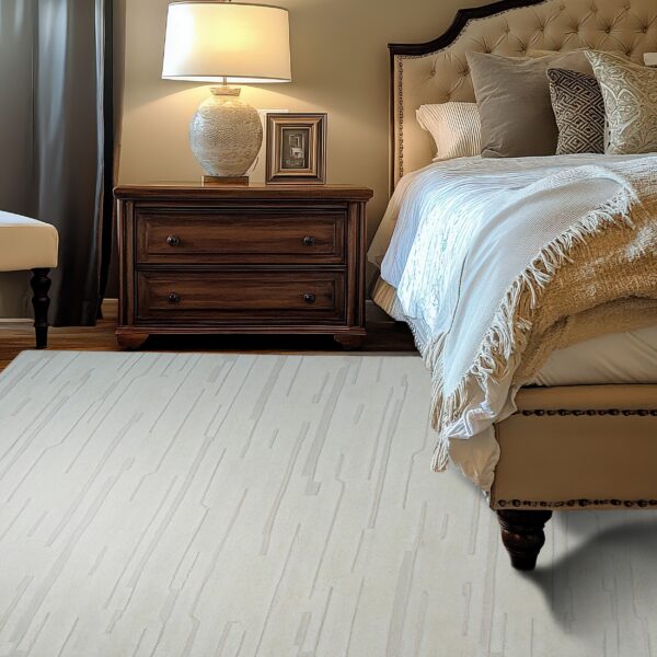 A cream area rug with subtle linear segments lies on hardwood in a classic bedroom setting.