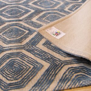 Textured blue and beige geometric rug, partially rolled back, revealing the woven underside and label.