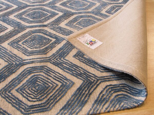 Textured blue and beige geometric rug, partially rolled back, revealing the woven underside and label.