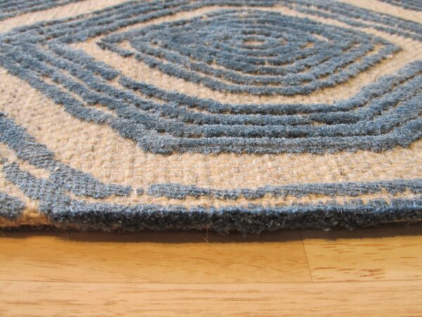 High-low pile rug with slate blue concentric diamond pattern on a natural beige field over wood flooring.
