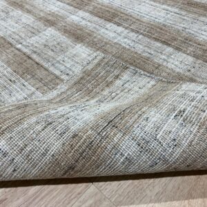 Tightly woven, speckled taupe and cream striped rug folded over on light wood flooring.