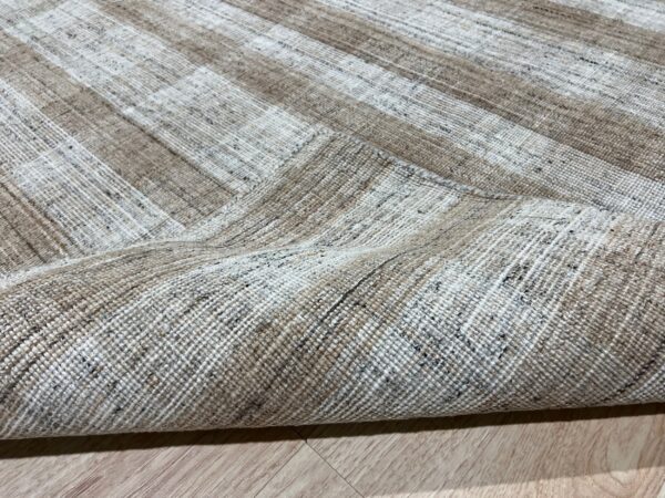 Tightly woven, speckled taupe and cream striped rug folded over on light wood flooring.