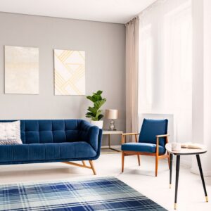 A blue and light gray tartan rug coordinates with a navy sofa in a brightly lit modern living room.