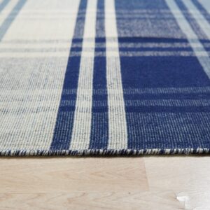 Detailed view of a flatweave rug with a blue, slate, and white striped plaid pattern on wood floor.