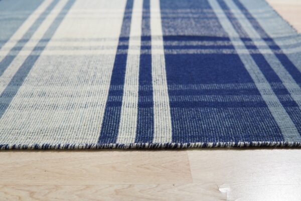 Detailed view of a flatweave rug with a blue, slate, and white striped plaid pattern on wood floor.