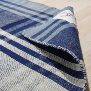 Partially rolled blue and off-white flatweave rug with a plaid pattern resting on a light wood floor.