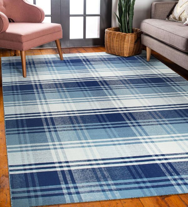 A blue, light blue, and white plaid rug lies on hardwood floors under pink and gray furniture.