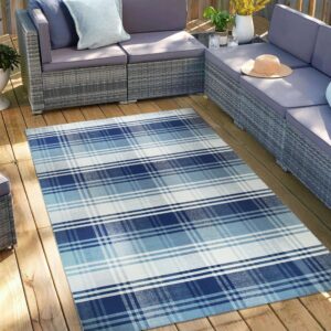 A flatwoven navy, blue, and white plaid rug covers a wooden deck under gray patio furniture.