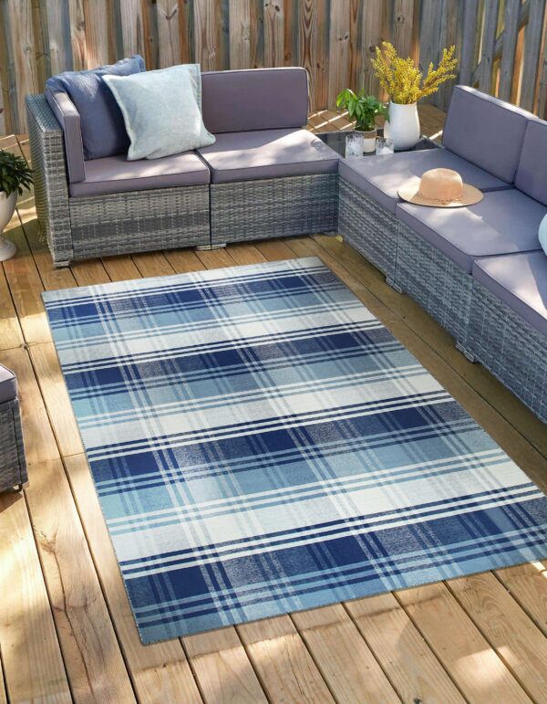 A flatwoven navy, blue, and white plaid rug covers a wooden deck under gray patio furniture.