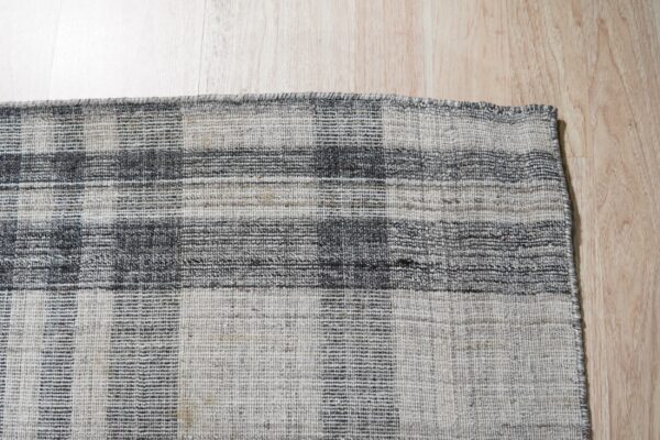 Low-pile grey and charcoal plaid rug visible on light wood plank flooring.