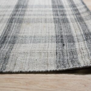 Close-up of a flatweave rug with a charcoal and light gray plaid pattern on light wood flooring.