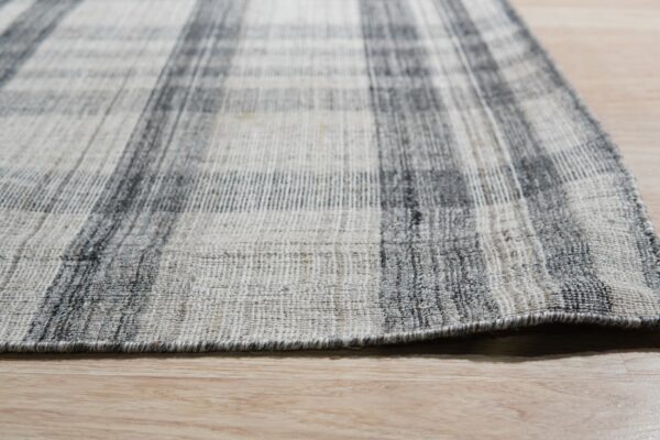Close-up of a flatweave rug with a charcoal and light gray plaid pattern on light wood flooring.