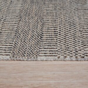 Textured rug with alternating cream stripes and dark geometric patterns resting on light wood flooring.