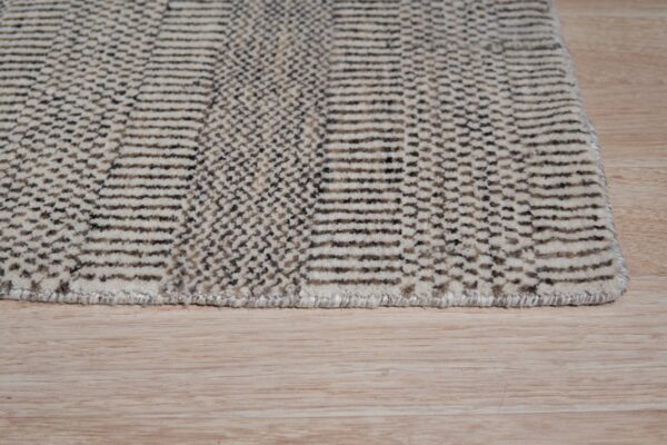 Textured rug with alternating cream stripes and dark geometric patterns resting on light wood flooring.