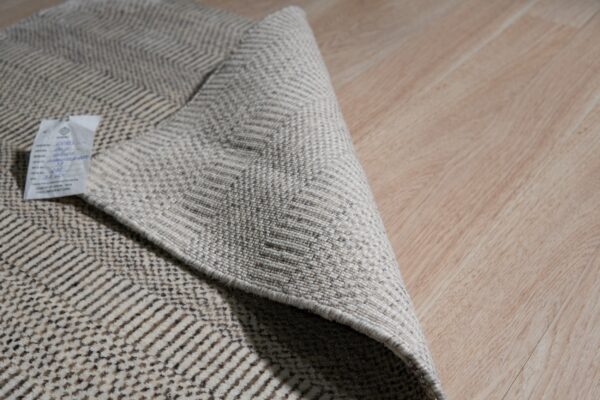 A low-pile beige rug with a dark chevron pattern is folded on a light wood floor.