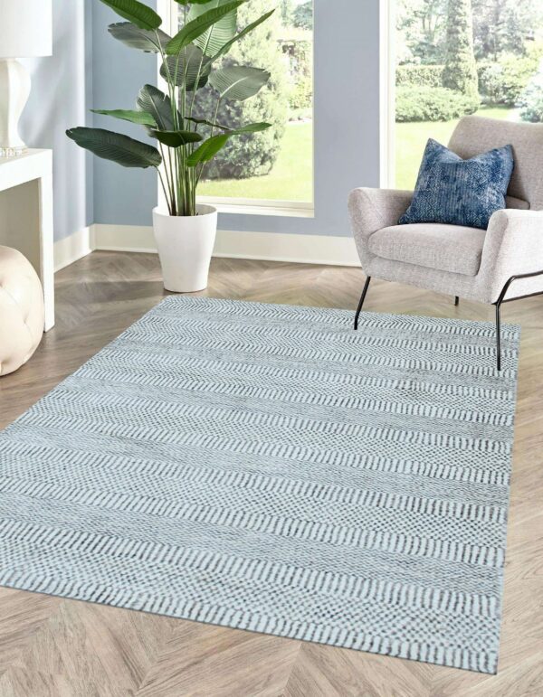 Pale blue striped rug with woven texture rests on light wood floors near a gray chair and window.