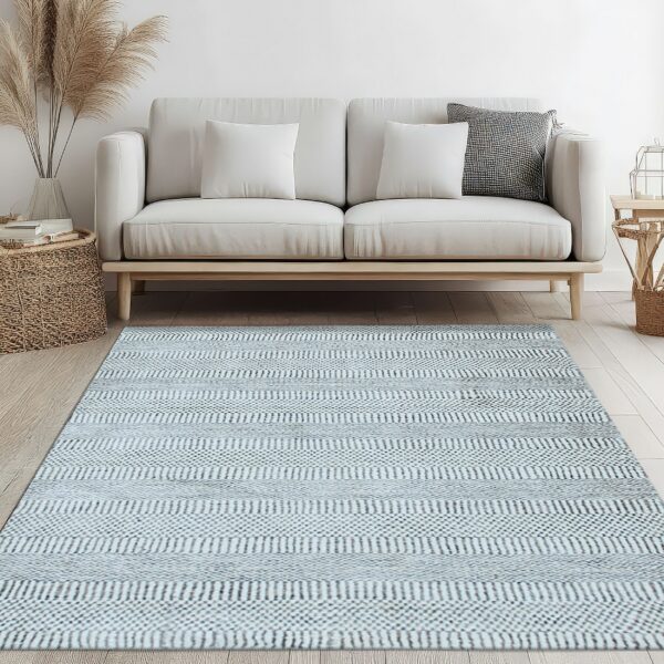 Woven light blue and gray striped rug underneath a cream sofa on light hardwood flooring.