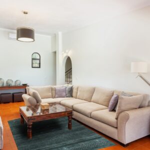 A teal, low-pile rug with small light patterns lies on orange tile under a light beige sectional sofa.
